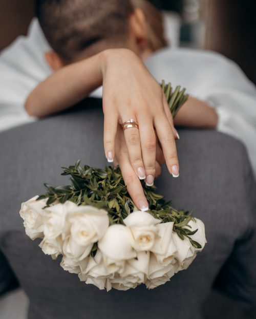 Bride's hands behind husband's head during a kiss. Gold wedding rings on fingers. Kiss of lovers and sensual embrace of a girl
